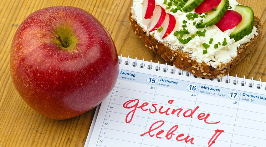 Ein Apfel und ein belegtes Brot liegen neben einem Zettel mit der Aufschritft: ,,gesünder leben''