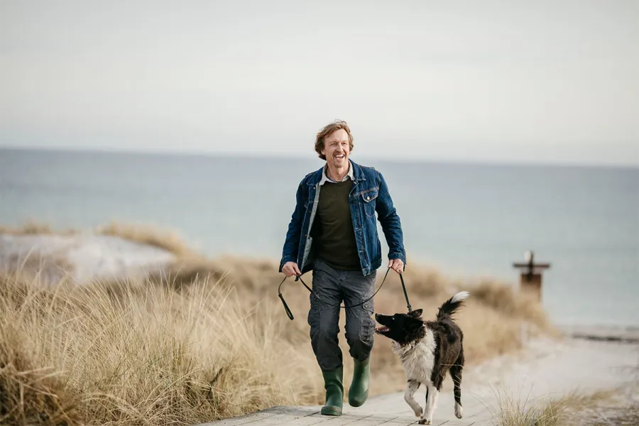 Mann spaziert mit Hund durch Dünen am Strand der Ostsee.