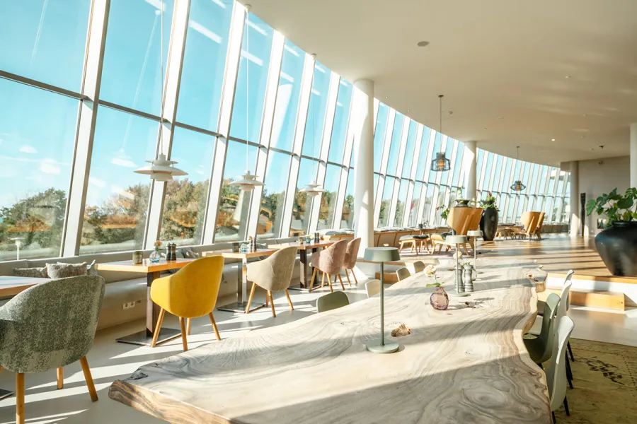 Heller Restaurantbereich mit großen Fensterfronten und Blick auf die Dünen an der Ostsee.