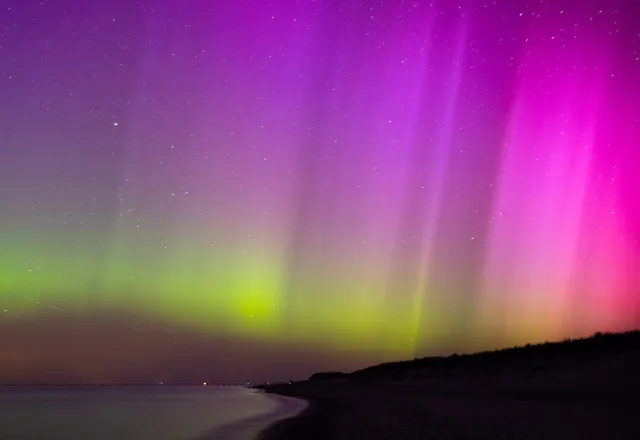 Leuchtende Nordlichter in Violett und Grün am sternenklaren Himmel über der Ostsee in Ahrenshoop.