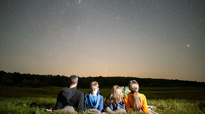 Familie liegt auf einer Wiese und blickt in den funkelnden Sternenhimmel.