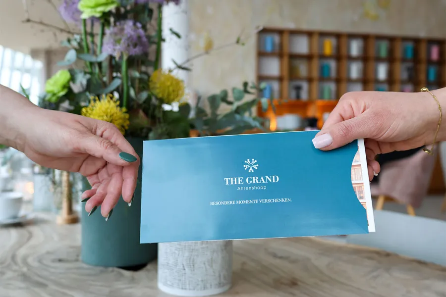 Hände überreichen einen Gutschein vom THE GRAND Ahrenshoop als Geschenk für einen Aufenthalt an der Ostsee