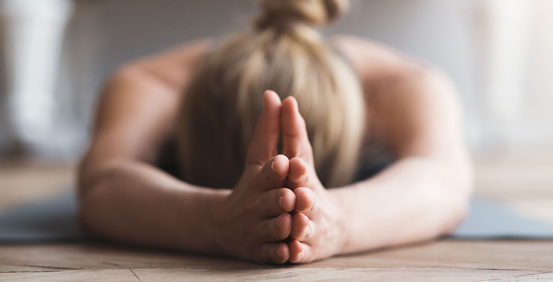 Person in ruhiger Yoga-Vorbeuge mit gefalteten Händen auf der Matte im THE GRAND Ahrenshoop.