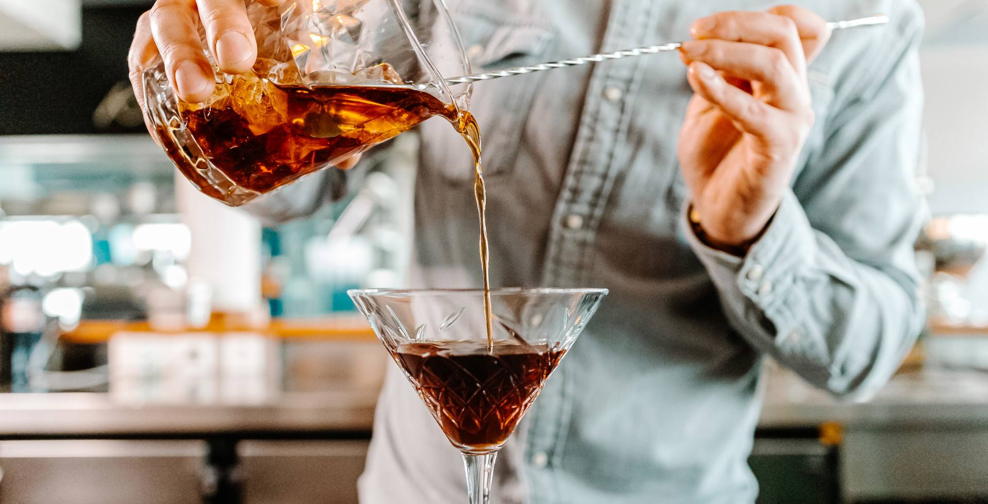 Ein Barkeeper gießt einen Cocktail in ein Glas und zeigt beim Cocktailworkshop im THE GRAND Ahrenshoop professionelle Mixtechniken