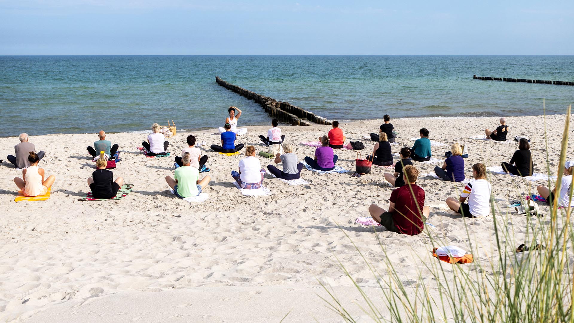 Pilateskurs des THE GRAND Ahrenshoop mit mehreren Teilnehmenden am Sandstrand von Ahrenshoop an der Ostsee.