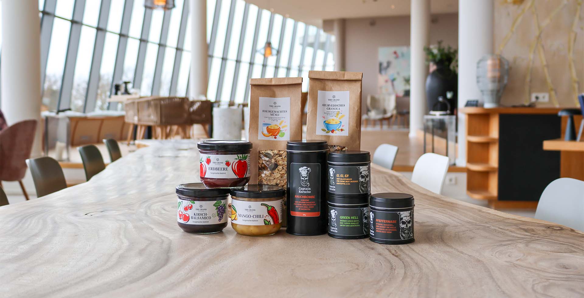 Gewürzmischungen, Fruchtaufstriche und zwei Sorten Müsli auf einem Holztisch präsentiert