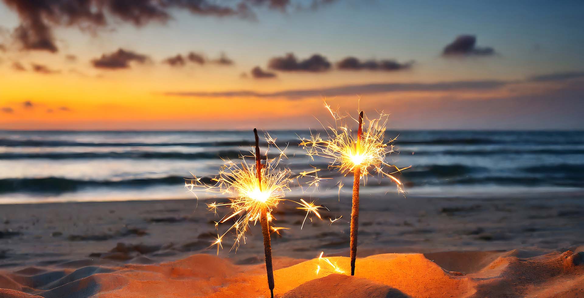Wunderkerzen leuchten im Sand am Strand bei Sonnenuntergang zu Silvester an der Ostsee.